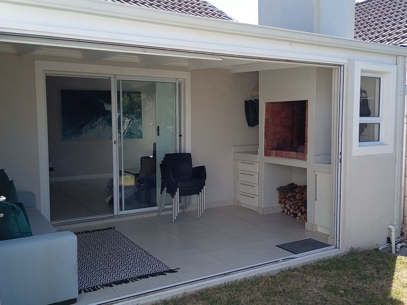 Covered patio area featuring a built-in brick braai, tiled flooring, and large stacking doors that provide seamless indoor-outdoor flow.