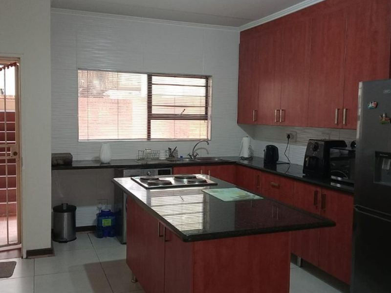 A functional kitchen featuring cherry-wood cabinetry, granite countertops, a central island with a built-in hob, and tiled flooring with direct access to an outdoor area.