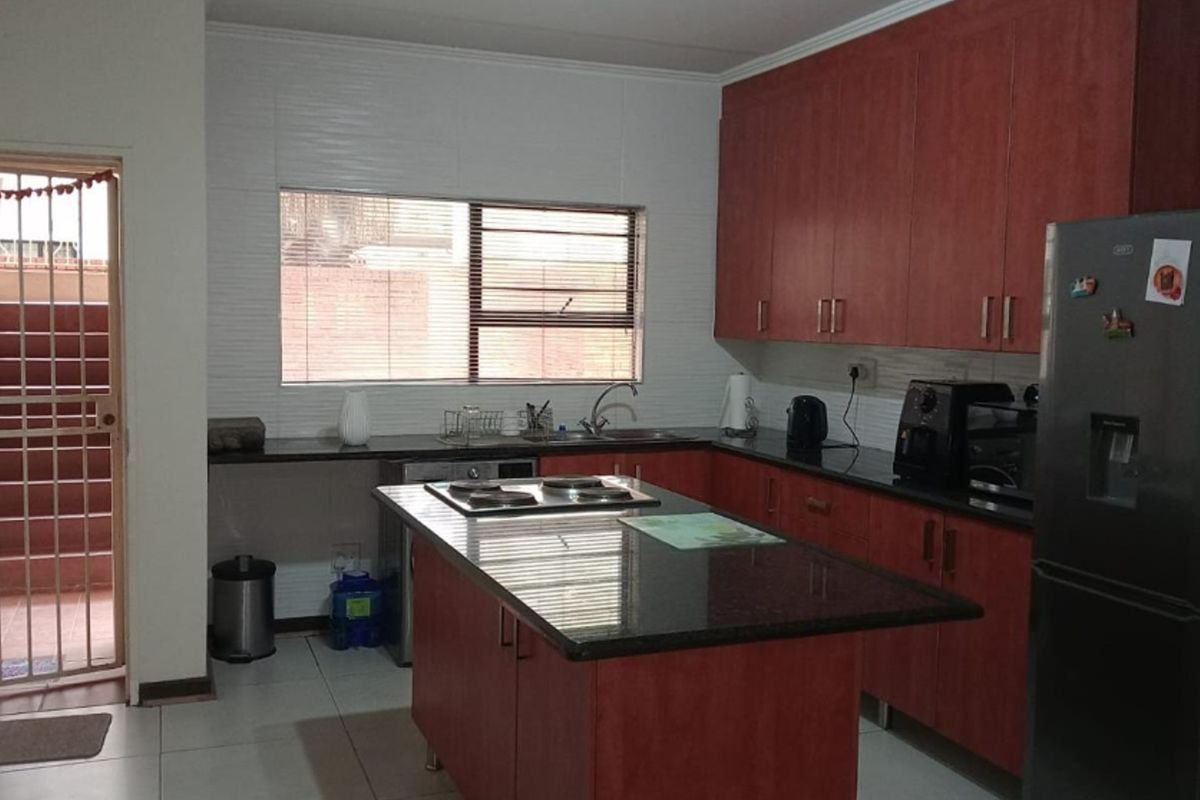 A functional kitchen featuring cherry-wood cabinetry, granite countertops, a central island with a built-in hob, and tiled flooring with direct access to an outdoor area.