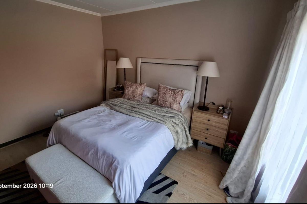 A neutrally painted bedroom featuring light-toned laminate flooring and large window access with curtain fixtures.