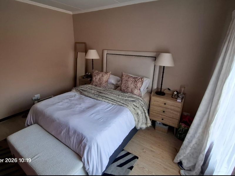 A neutrally painted bedroom featuring light-toned laminate flooring and large window access with curtain fixtures.
