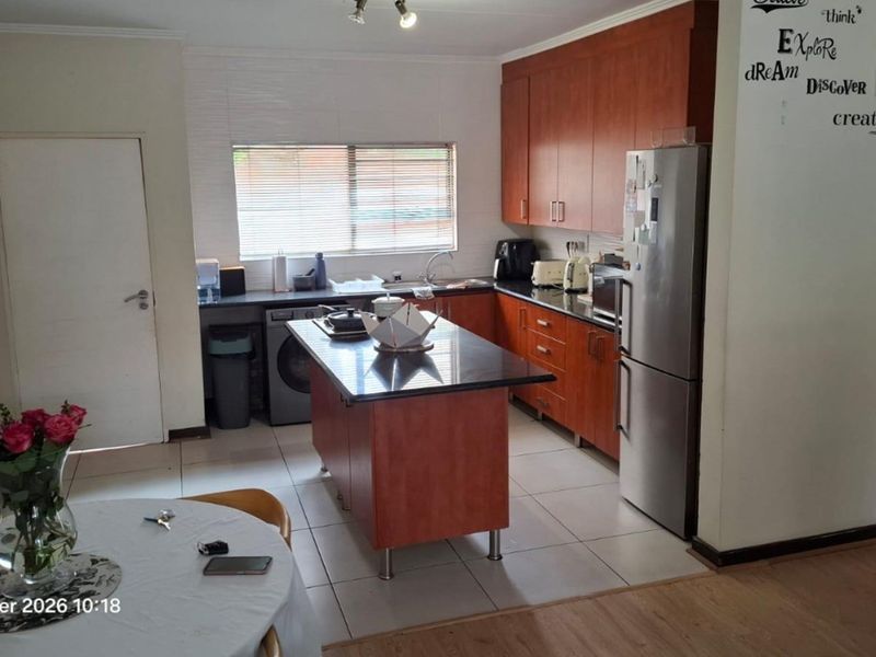 A functional kitchen featuring wood-finish cabinetry, a central island with stone countertops, tiled flooring, and integrated space for appliances.