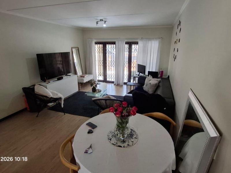 A spacious living and dining area featuring light laminate flooring and large sliding doors with security gates leading to an outdoor space.