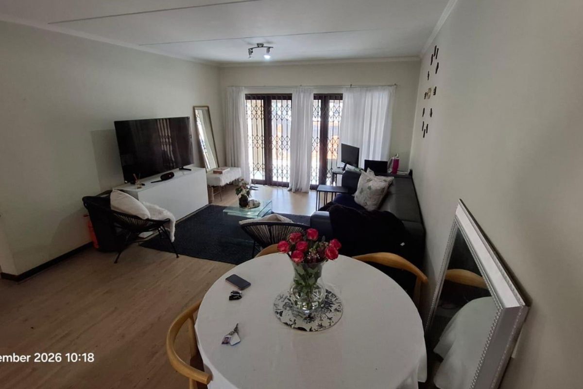 A spacious living and dining area featuring light laminate flooring and large sliding doors with security gates leading to an outdoor space.