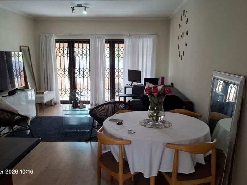 Open plan living and dining area featuring laminate flooring and sliding doors with security gates leading to the exterior.