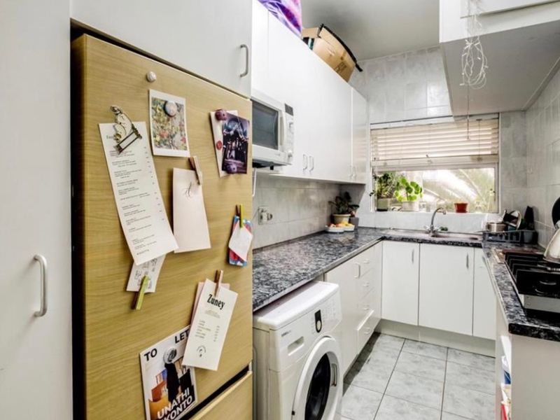 Compact kitchen featuring white cabinetry, granite countertops, tiled backsplash, and integrated appliances including a gas hob and built-in oven.