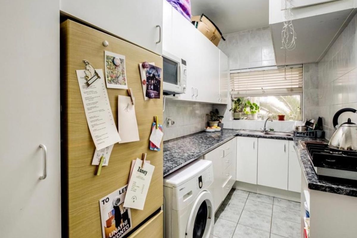 Compact kitchen featuring white cabinetry, granite countertops, tiled backsplash, and integrated appliances including a gas hob and built-in oven.