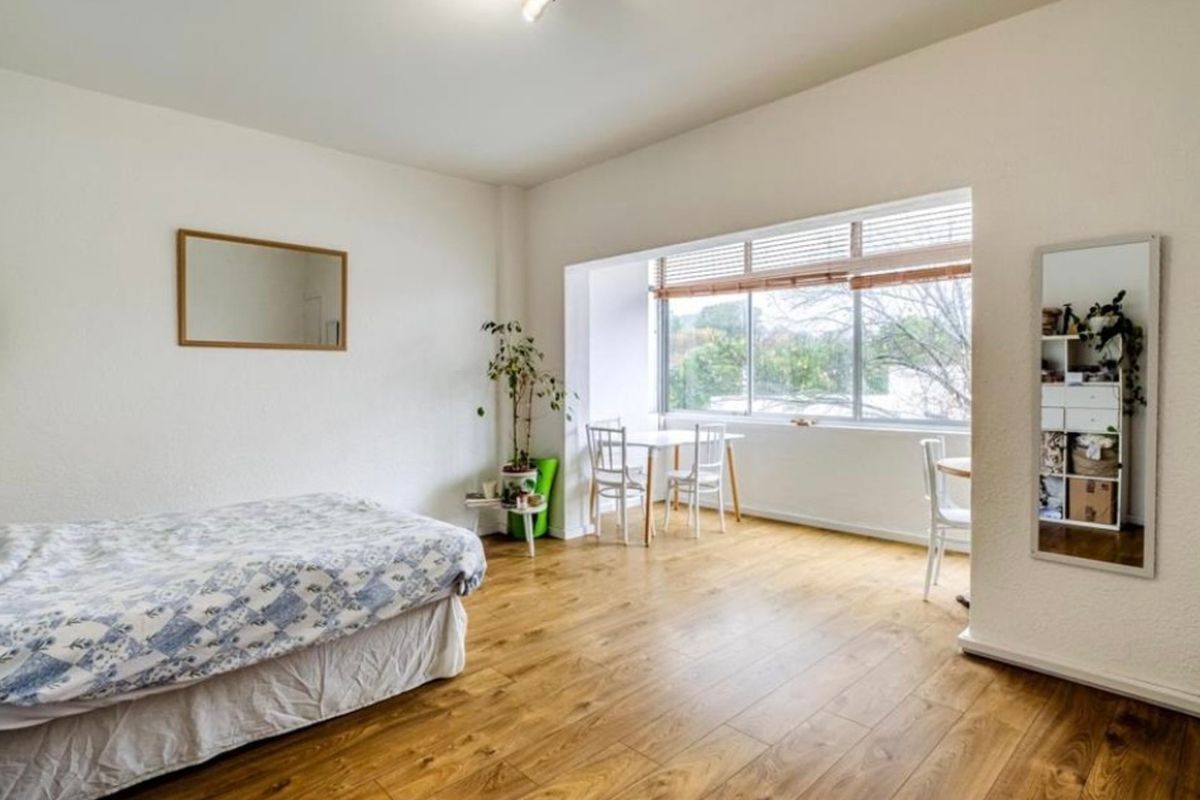 A spacious bedroom featuring durable laminate flooring and a large window with venetian blinds, offering ample natural light.