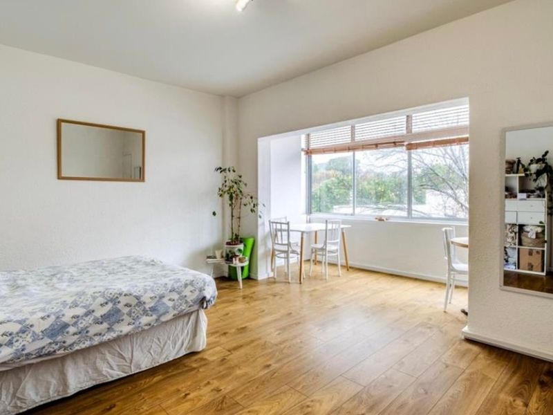 A spacious bedroom featuring durable laminate flooring and a large window with venetian blinds, offering ample natural light.