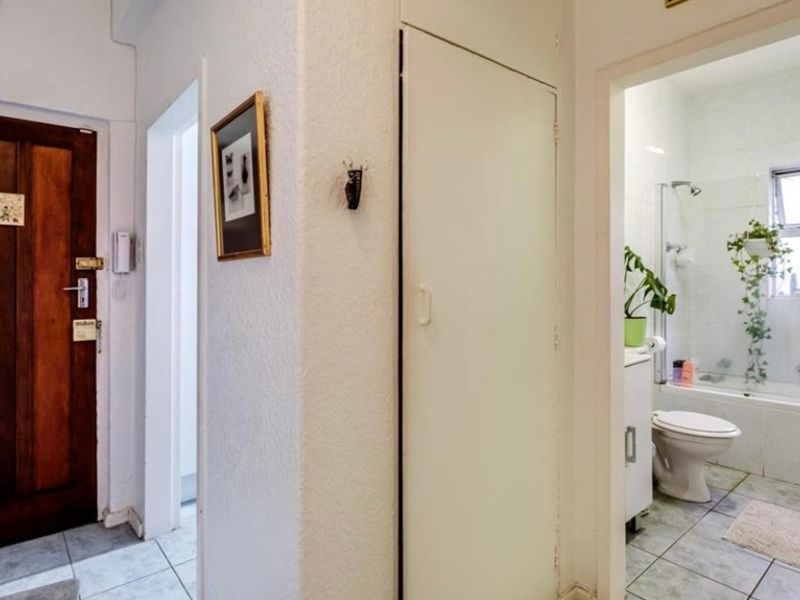 A functional hallway featuring tiled flooring, a solid wood entrance door, and a built-in storage cupboard, providing access to the adjacent bathroom.