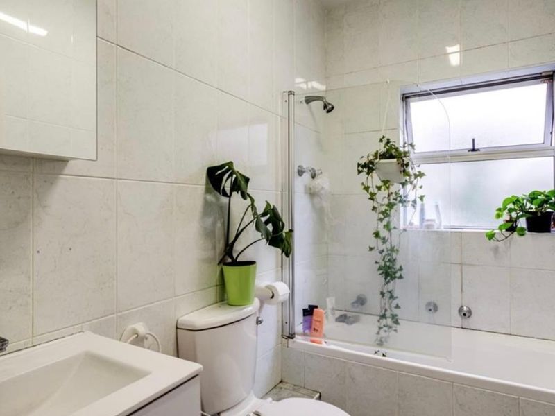 A functional bathroom featuring a built-in vanity, toilet, and a combined bathtub and shower with a glass screen and tiled finishes.