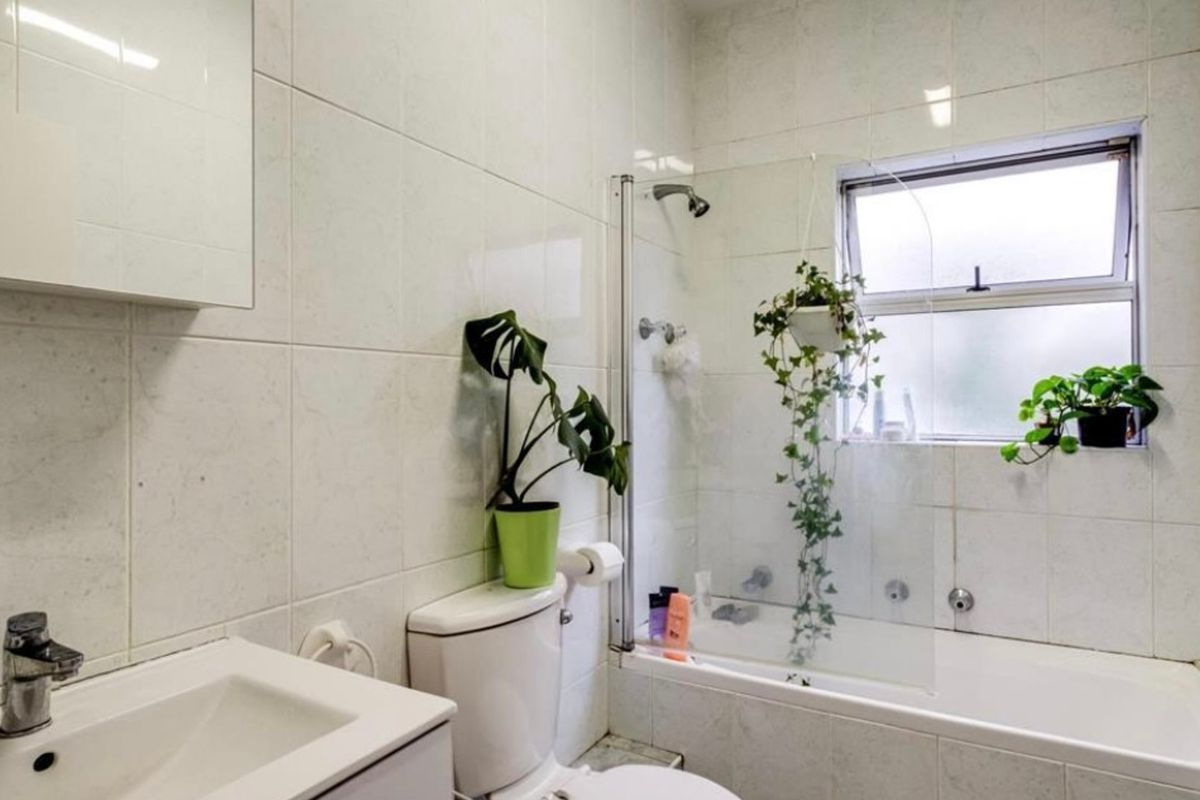 A functional bathroom featuring a built-in vanity, toilet, and a combined bathtub and shower with a glass screen and tiled finishes.