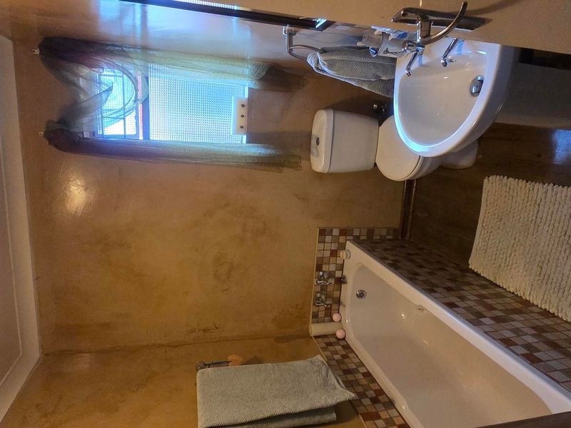 A compact bathroom featuring a pedestal basin, toilet, and a bathtub with mosaic tile detailing, requiring cosmetic updates to modernize the space.