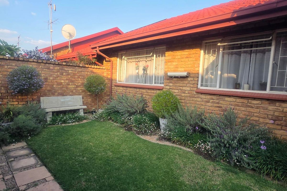 A well-maintained rear garden area featuring a face brick facade, red tiled roof, and a paved walkway alongside a small lawn.