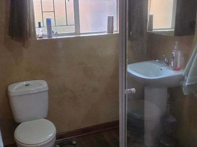 A compact bathroom featuring a pedestal basin, toilet, and a shower enclosure with a window providing natural light.