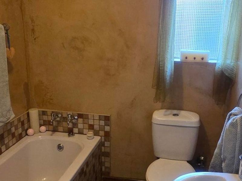 A compact bathroom featuring a bathtub with mosaic tile splashback, a standard toilet, and an obscured glass window for privacy.