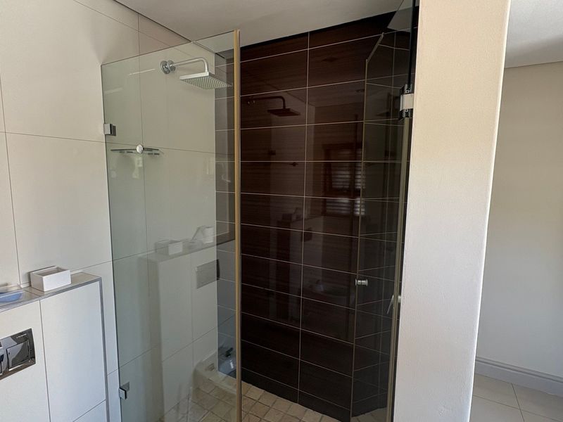 Modern bathroom featuring a glass-enclosed shower with a rain shower head and contrasting dark tiled accent wall.