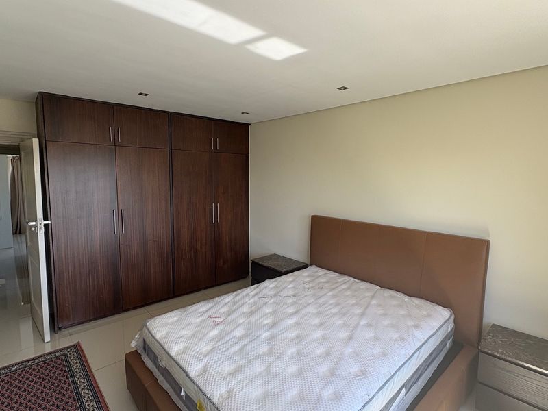 A well-maintained bedroom featuring dark wood built-in cupboards, neutral wall finishes, recessed downlighting, and polished floor tiles.