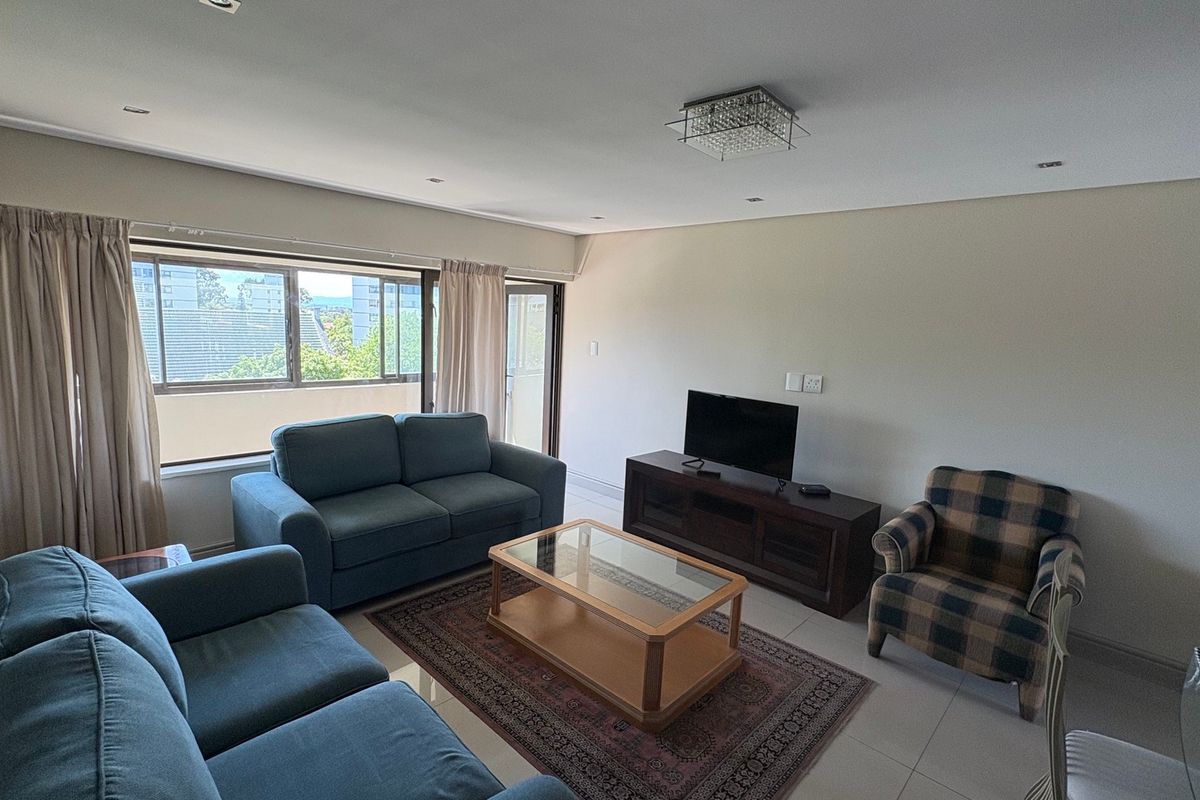A bright and spacious living room featuring tiled flooring, recessed downlighting, and large windows that provide natural light and access to an outdoor area.
