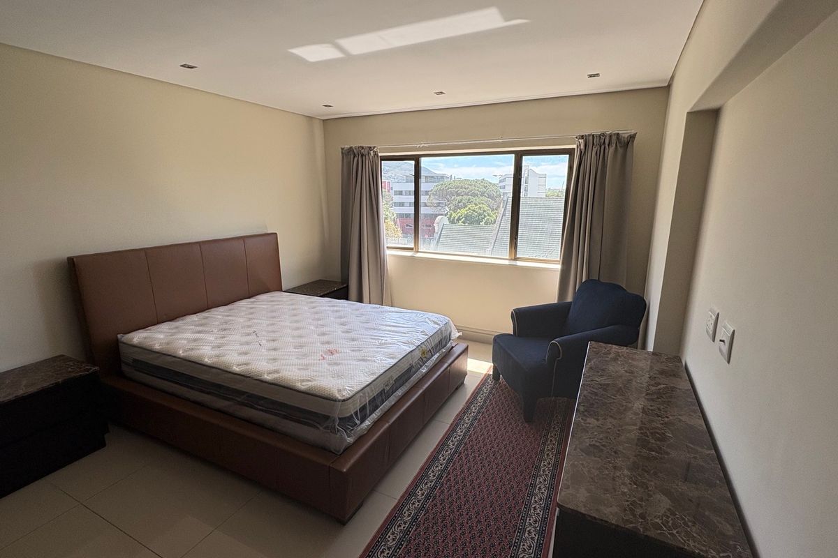 A spacious bedroom featuring tiled flooring, recessed downlighting, and a large window providing natural light and an urban view.