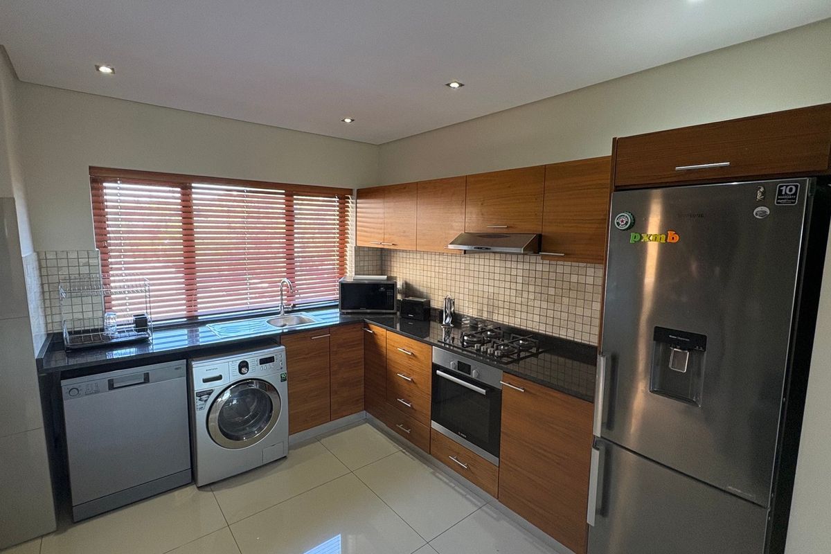 Modern kitchen featuring wood-finish cabinetry, granite countertops, integrated gas hob, oven, extractor fan, and tiled flooring with ample natural light.