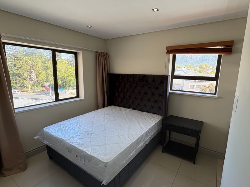 A bright bedroom featuring tiled flooring, recessed downlighting, and dual windows offering natural light and neighbourhood views.