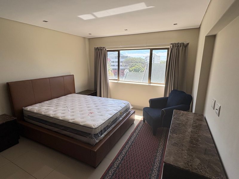 A spacious bedroom featuring tiled flooring, recessed downlighting, and a large window providing natural light and an urban view.