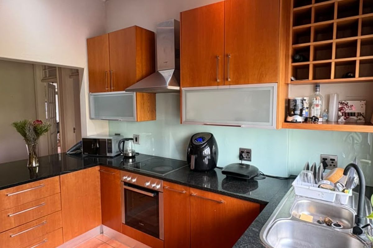 A functional kitchen featuring warm-toned wooden cabinetry, granite countertops, a glass splashback, and integrated stainless steel appliances including an oven and extractor fan.