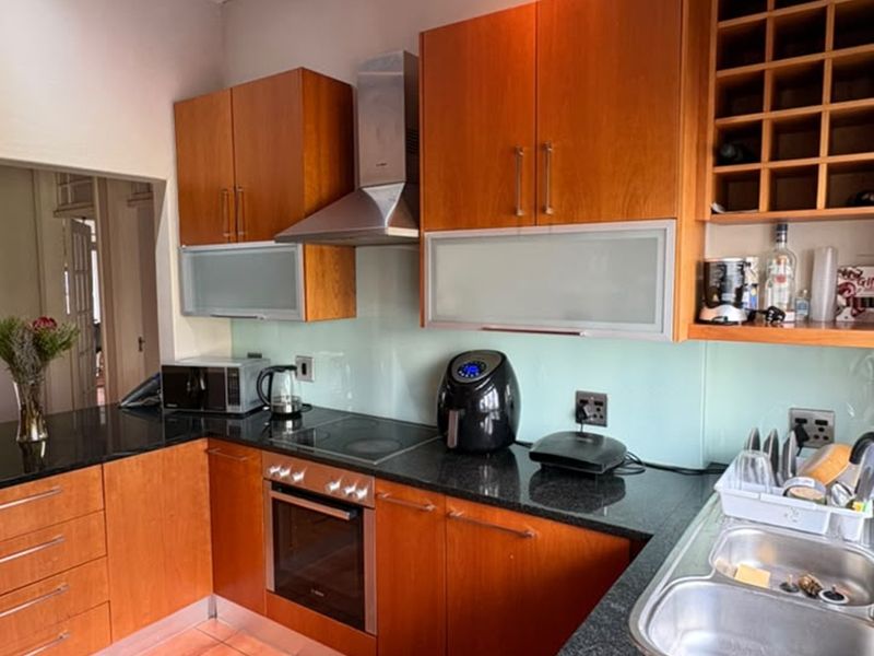 A functional kitchen featuring warm-toned wooden cabinetry, granite countertops, a glass splashback, and integrated stainless steel appliances including an oven and extractor fan.
