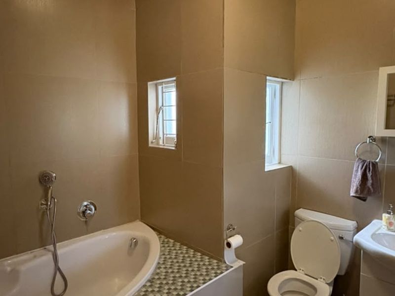A functional bathroom featuring a bathtub with handheld shower, pedestal basin, and toilet, finished with neutral wall tiles and a mosaic-tiled bath surround.