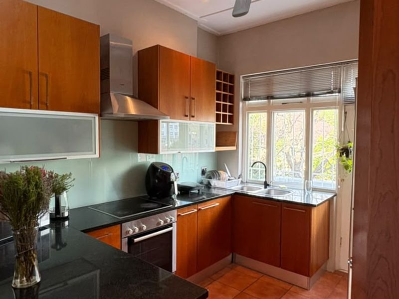 A functional kitchen featuring warm wooden cabinetry, granite countertops, a built-in oven with hob, and a double sink with natural light.