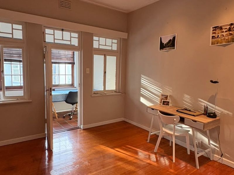 A bright bedroom featuring polished timber flooring, classic casement windows with transom detailing, and direct access to an adjoining balcony space.