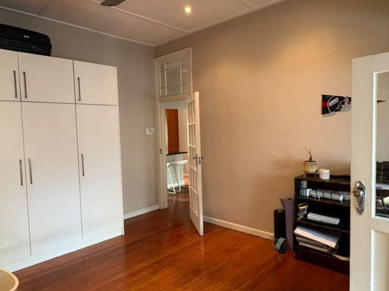 A bedroom featuring polished hardwood flooring, a large built-in wardrobe, and a ceiling fan, with a view through a doorway into an adjacent space.
