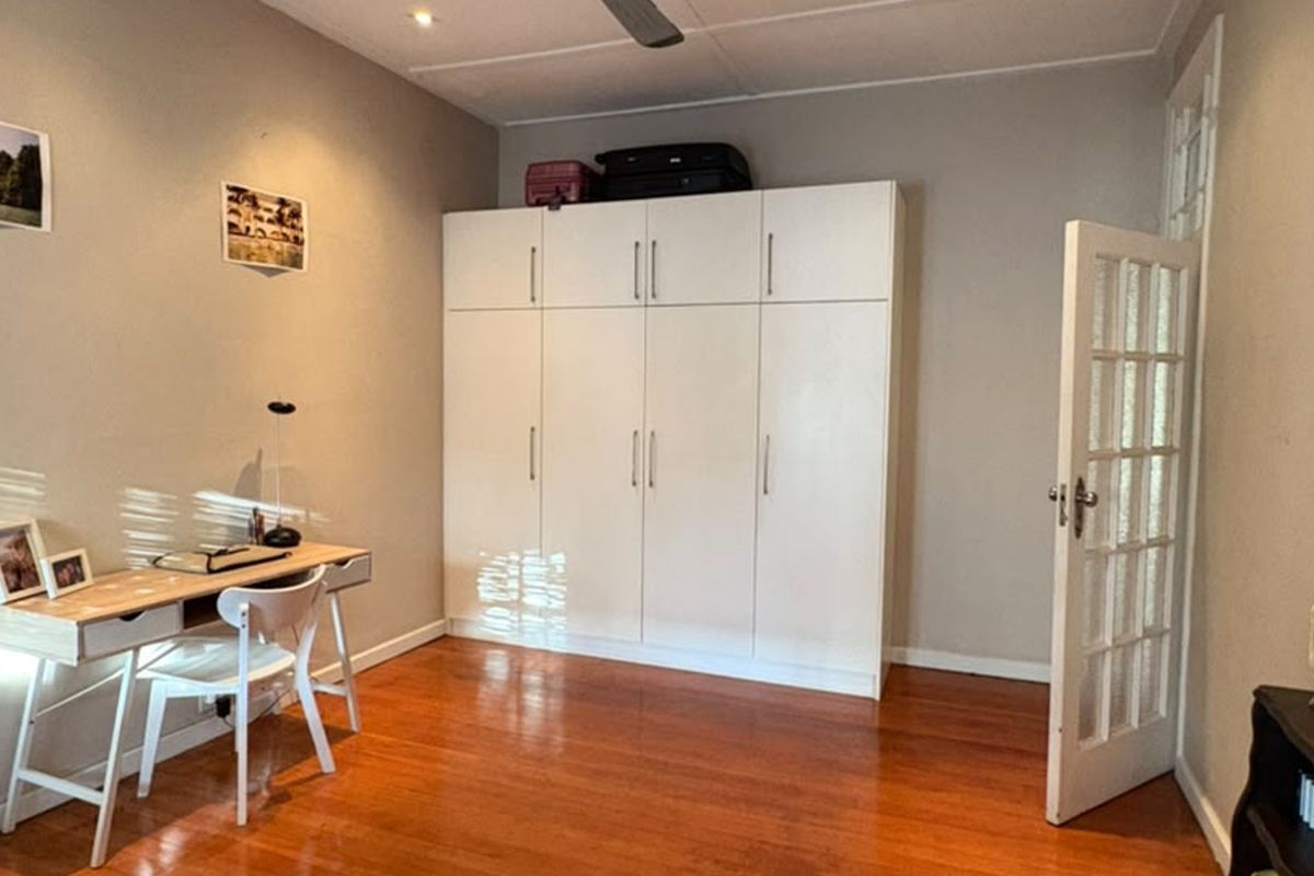 A bedroom featuring polished hardwood flooring, a large white built-in wardrobe, and a classic french door entrance.