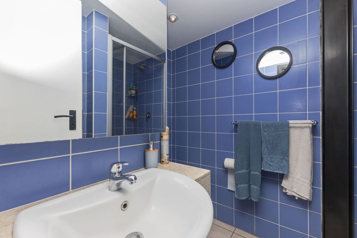 A functional bathroom featuring blue wall tiles, a vanity basin with chrome mixer tap, a large wall mirror, and a glass shower enclosure.