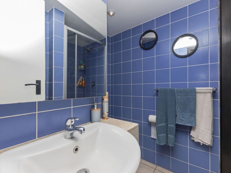 A functional bathroom featuring blue wall tiles, a vanity basin with chrome mixer tap, a large wall mirror, and a glass shower enclosure.