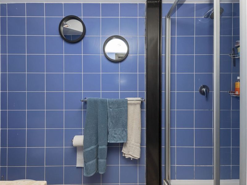 A functional bathroom featuring blue wall tiling, a shower enclosure, and a standard toilet, offering a clean and practical layout.