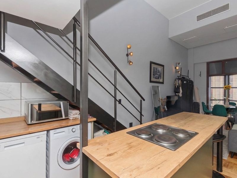 Open-plan living area featuring a modern kitchen island with integrated hob, parquet flooring, and a striking industrial-style staircase leading to the upper level.