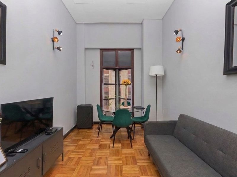 A well-maintained living area featuring classic parquet flooring, neutral wall finishes, and wall-mounted lighting, creating a comfortable and functional space.