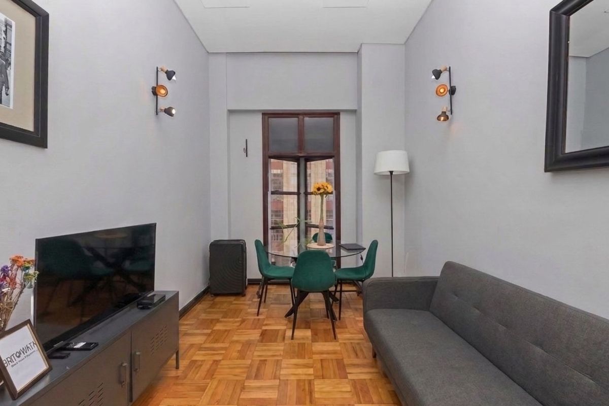A well-maintained living area featuring classic parquet flooring, neutral wall finishes, and wall-mounted lighting, creating a comfortable and functional space.