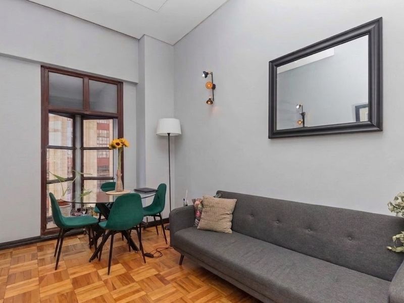 A well-maintained living area featuring classic parquet flooring, neutral wall tones, and a large window providing natural light and urban views.