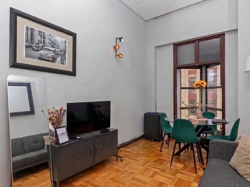 A well-lit living area featuring classic parquet flooring, neutral walls, and a large window that provides natural light and an urban view.