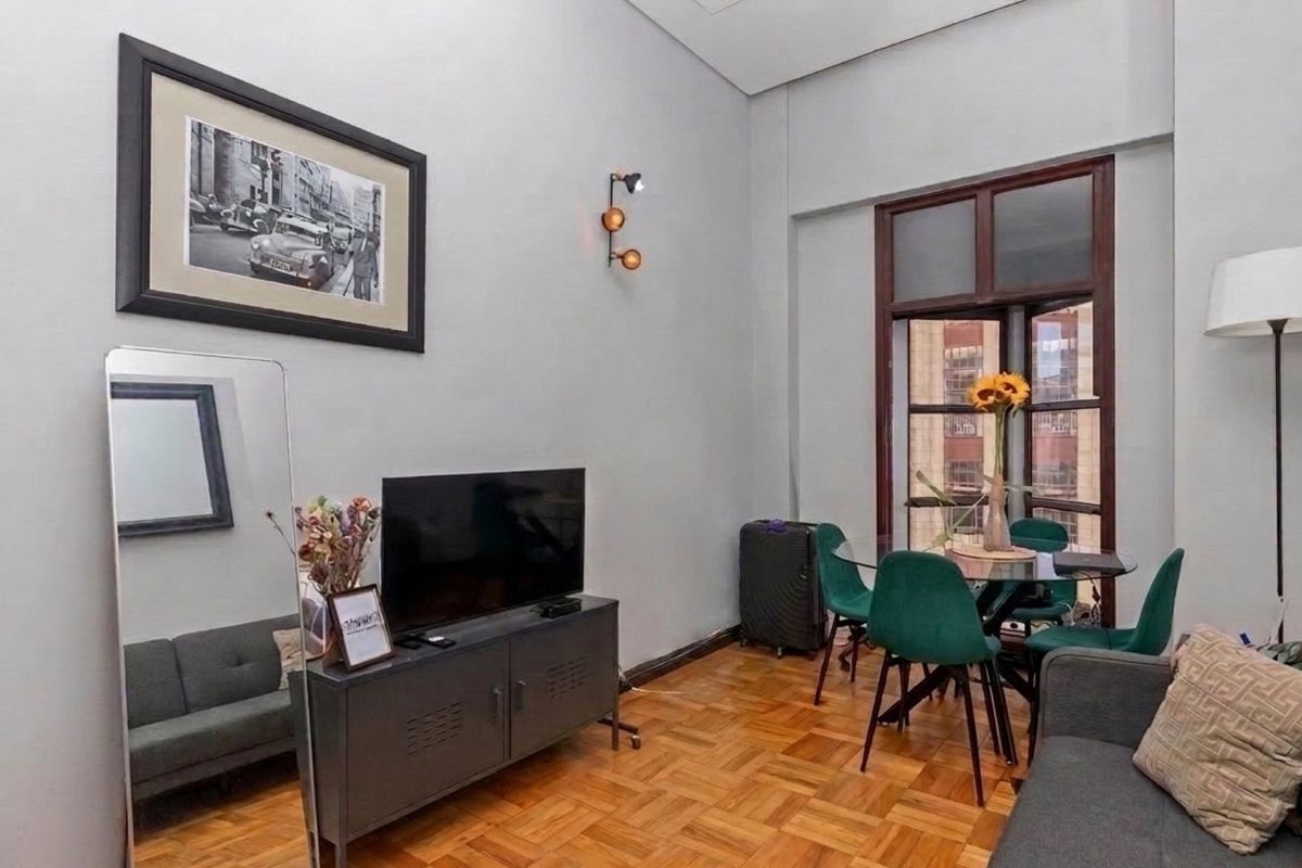 A well-lit living area featuring classic parquet flooring, neutral walls, and a large window that provides natural light and an urban view.