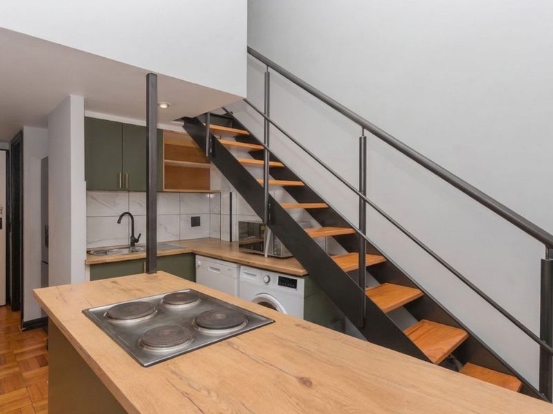 Modern open-plan kitchen featuring a built-in hob, sleek cabinetry, and a striking staircase with metal handrails, set against warm parquet flooring.