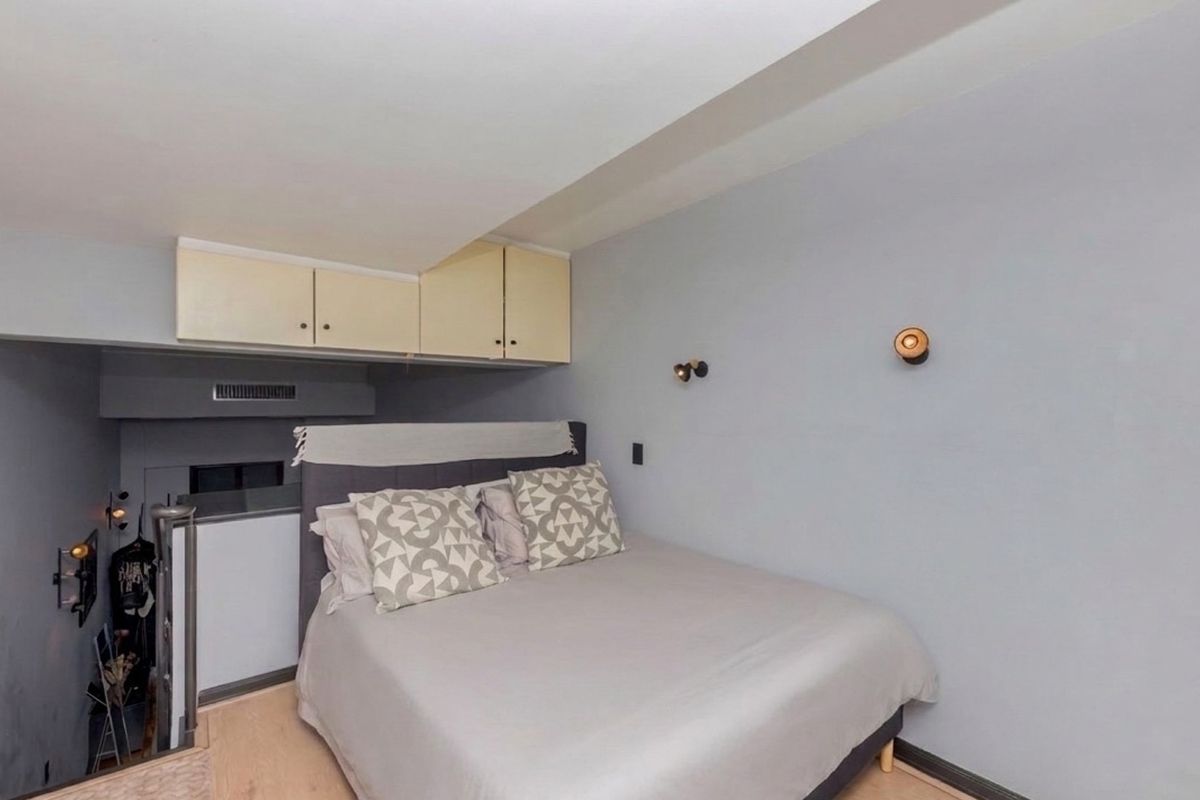 A compact bedroom featuring built-in overhead storage cabinets, wall-mounted lighting, and direct access to a staircase.