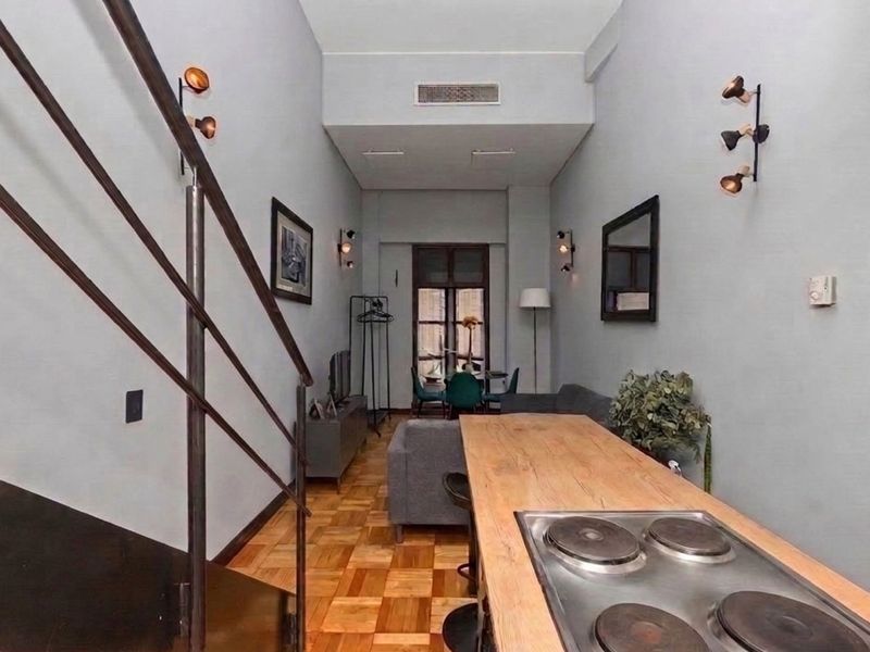 An open-plan living and kitchen area featuring parquet flooring, a built-in hob, and a staircase with a metal railing.