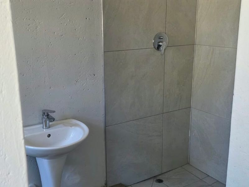 A compact bathroom featuring a pedestal basin with a mixer tap and a tiled shower enclosure with a wall-mounted mixer.