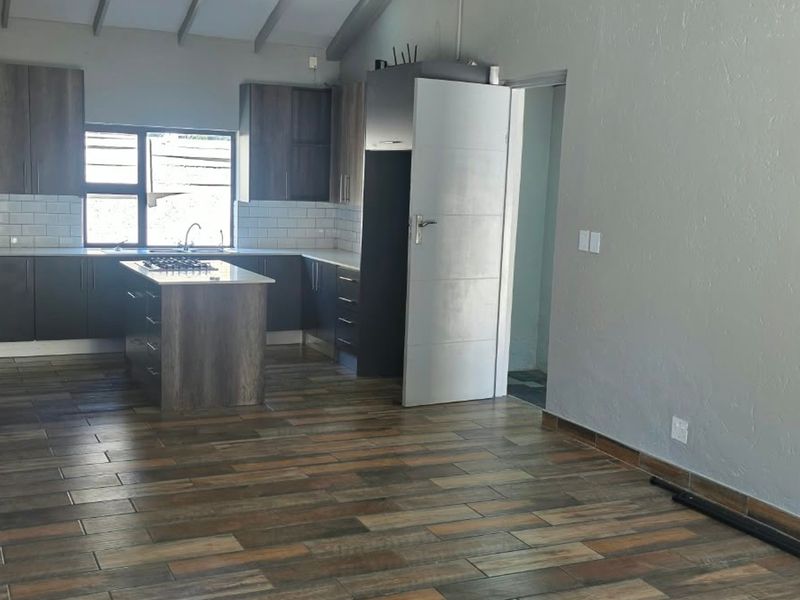 Spacious open-plan kitchen featuring modern dark cabinetry, a central island with a gas hob, subway tile backsplash, and durable timber-look floor tiles.