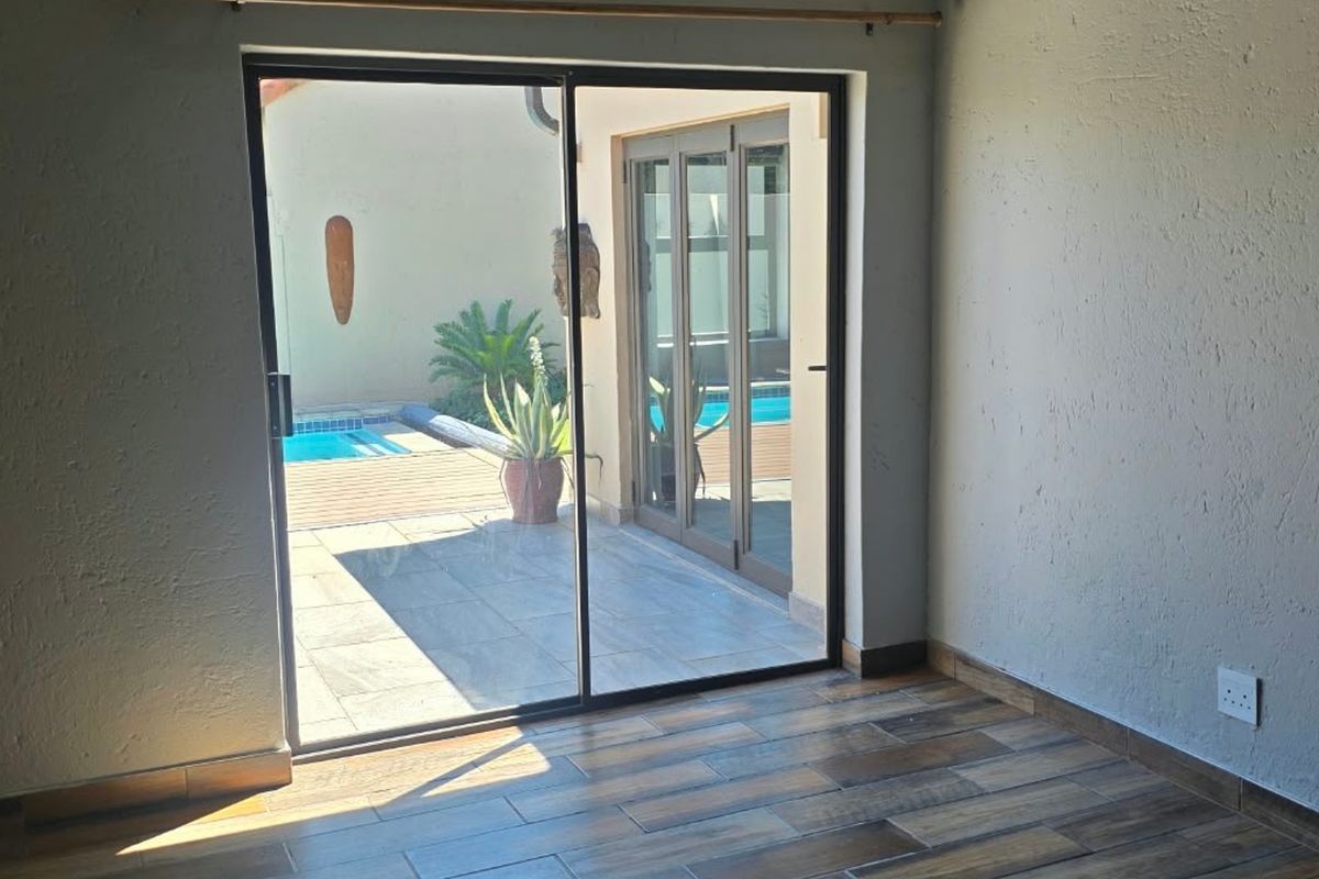 An empty living room featuring modern wood-look tiled flooring and a large sliding glass door providing direct access to the patio and pool area.