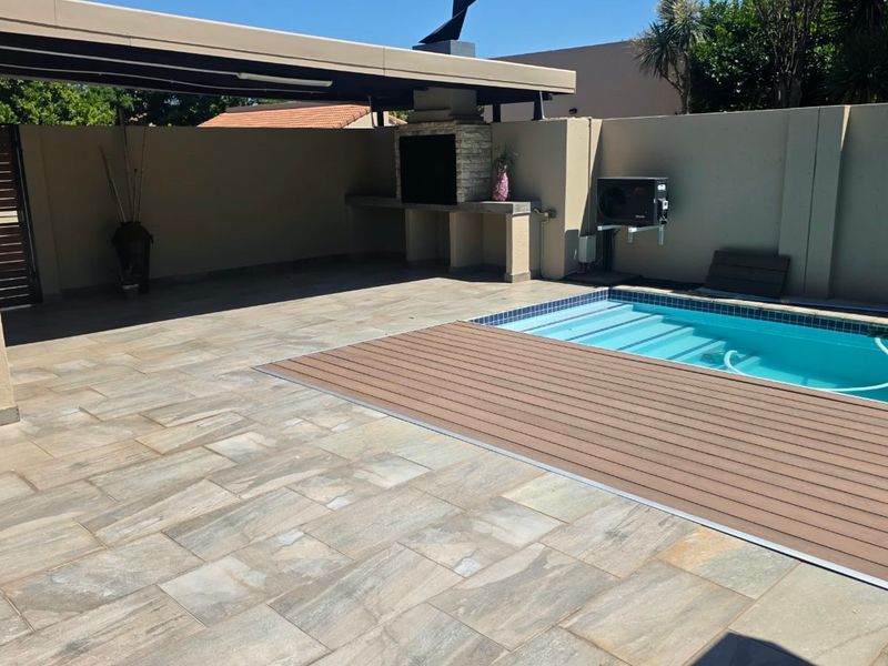 Outdoor entertainment area featuring a swimming pool with composite decking, a covered patio, and a built-in braai, set within a private walled garden.